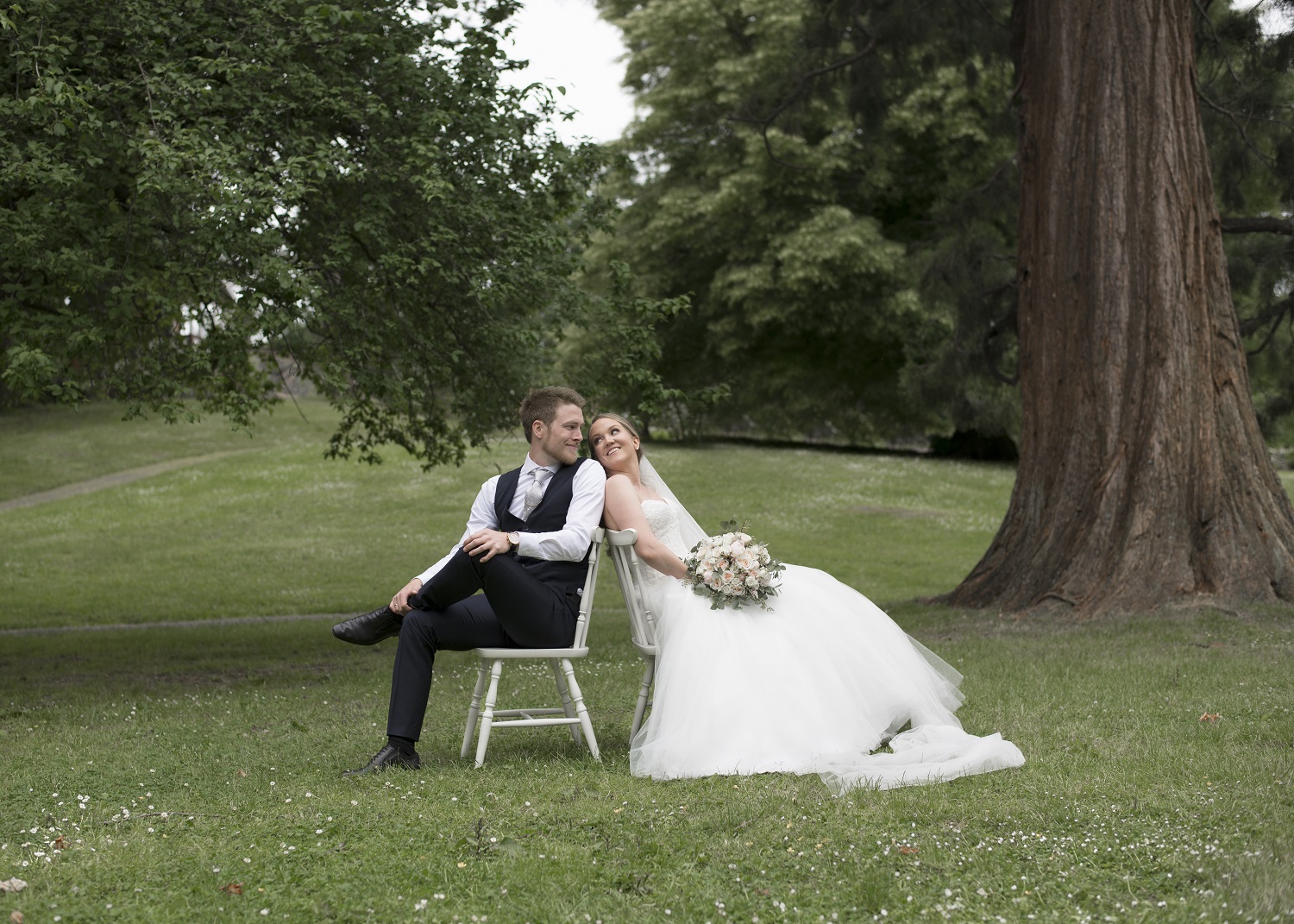 Brudepar sitte under treet på hvite stoler